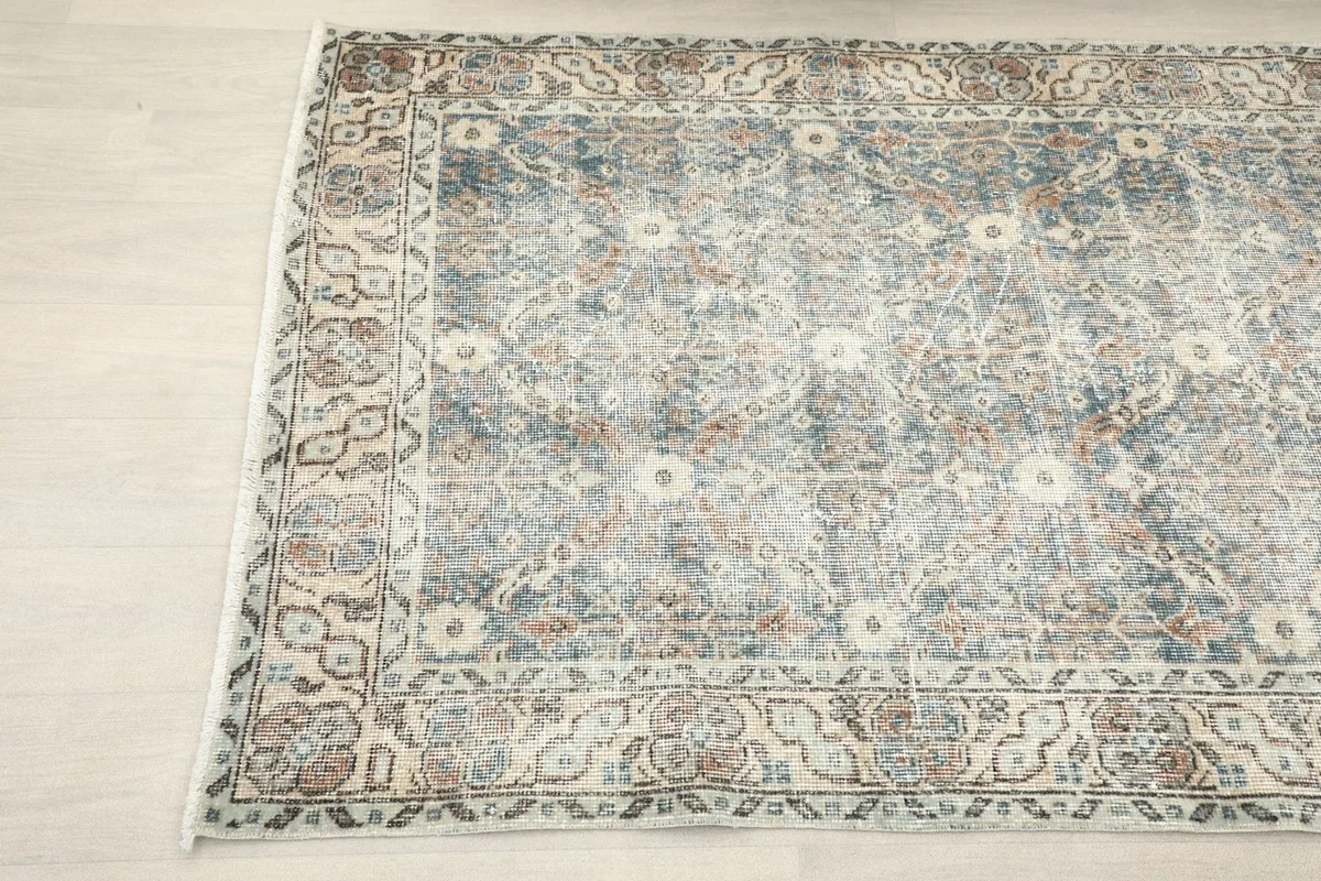 Angled view of the vintage area rug, showing its soft colors and detailed border