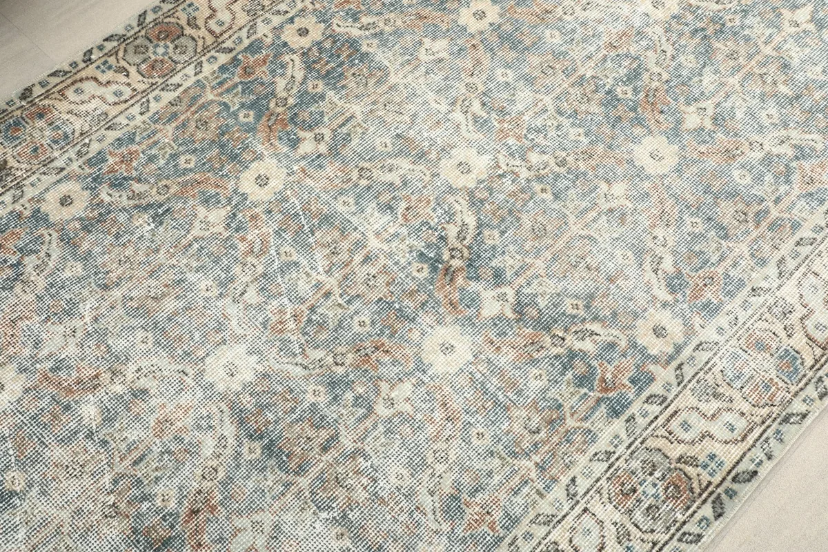 Detailed view of the rug's central field with muted blue, beige, and brown floral motifs