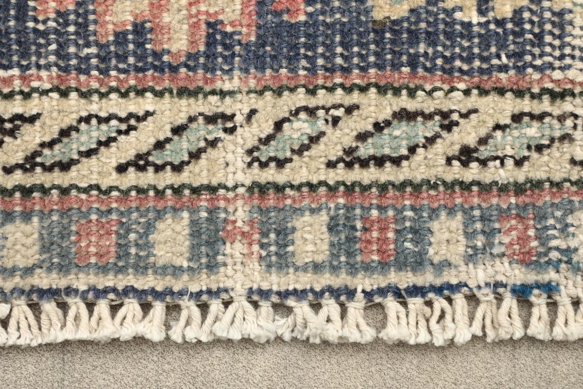 Close-up of the rug's border pattern in navy, beige, and light blue with fringe