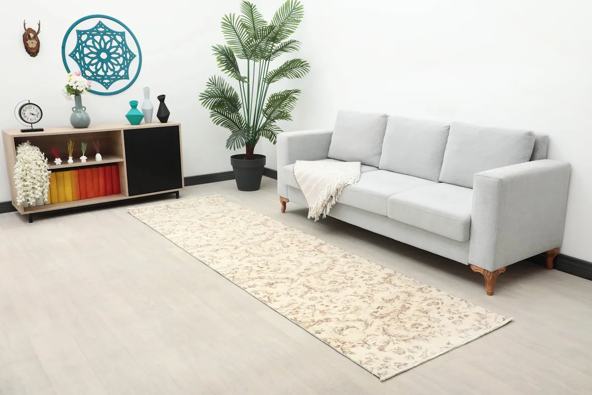 Long shot of the ivory and tan runner rug in a room with a sofa, plant, and decorative shelf.