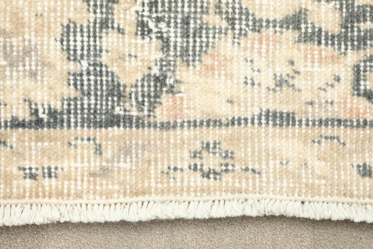 Close-up view of the rug's border and fringe, showing the low pile texture and faded colors