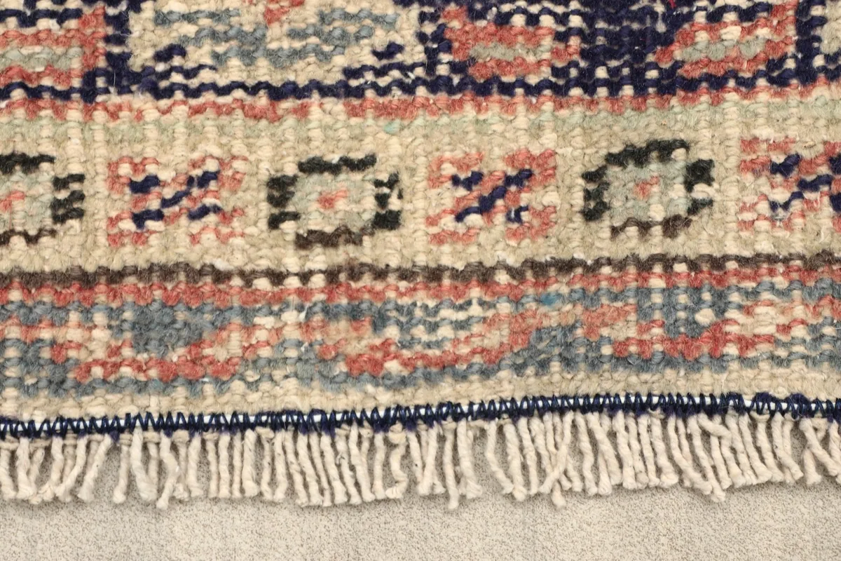 Close-up detail of the short fringe and intricate border patterns of the vintage rug