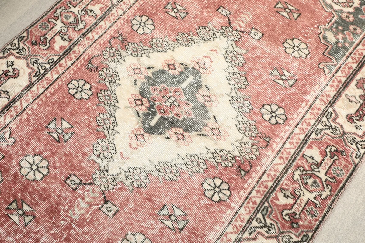 Detailed view of the rug's surface, capturing the subtle variations in its vintage rose and ivory colors.
