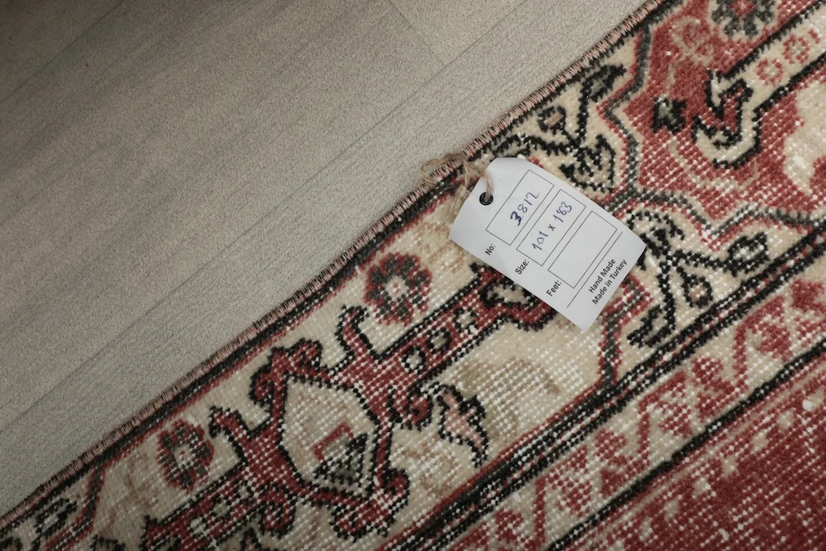 View of the rug's back corner with a size tag, showing the tightly woven cotton foundation.