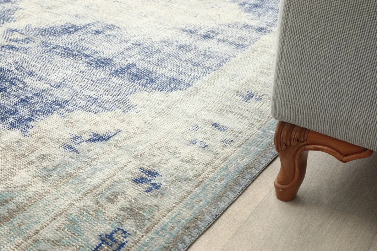 Close-up of the rug's edge next to a sofa leg, showing pile height and subtle color variations