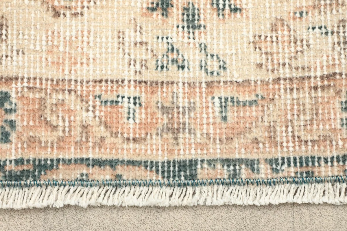 Close-up of the rug's fringe and a section of the border pattern in tan, blue, and ivory