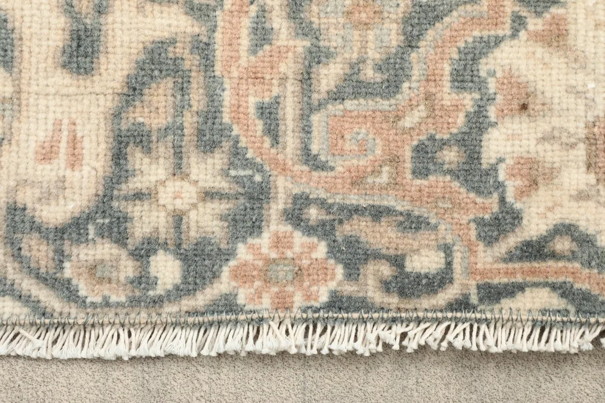 Close-up view of the rug's fringe and a section of the border with blue and rust patterns
