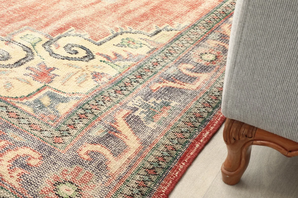 Close-up of the rug next to furniture, showing the border design and texture in a room