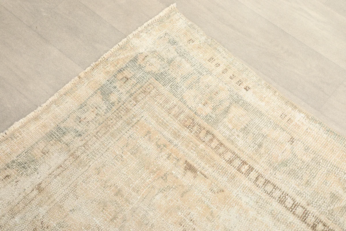Corner detail of the rug, showing the faded blue and tan border elements against the beige field.