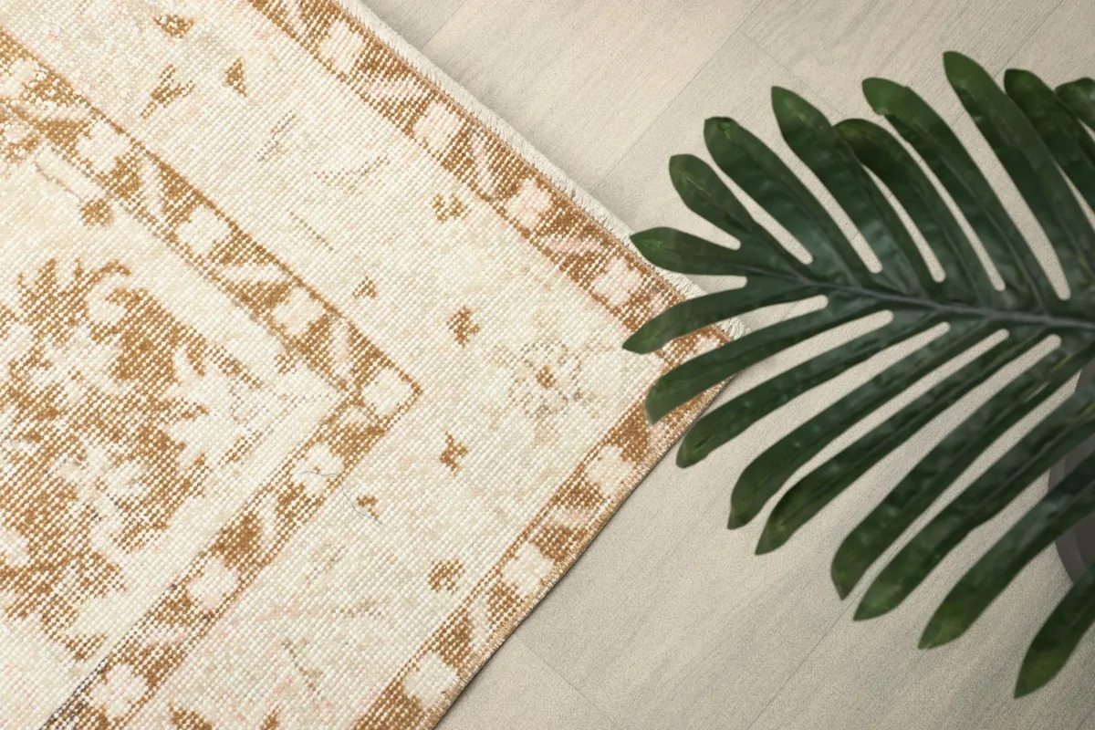 Corner of the rug with a plant, showing the tan border and subtle pattern