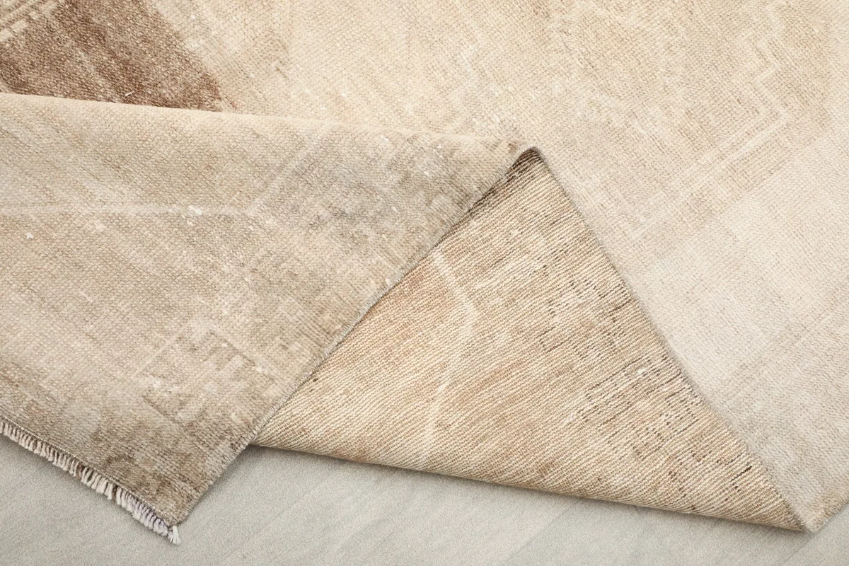 View of the back of the rug where a corner is folded, showing the cotton foundation and knotting.
