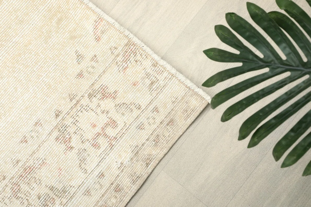 Corner of the rug with a green leaf, emphasizing the soft ivory and rose colors