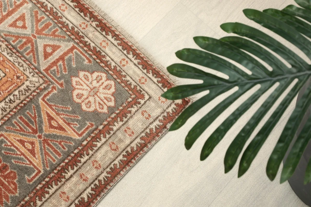 Angled view of the rug's border with a green plant leaf in the foreground