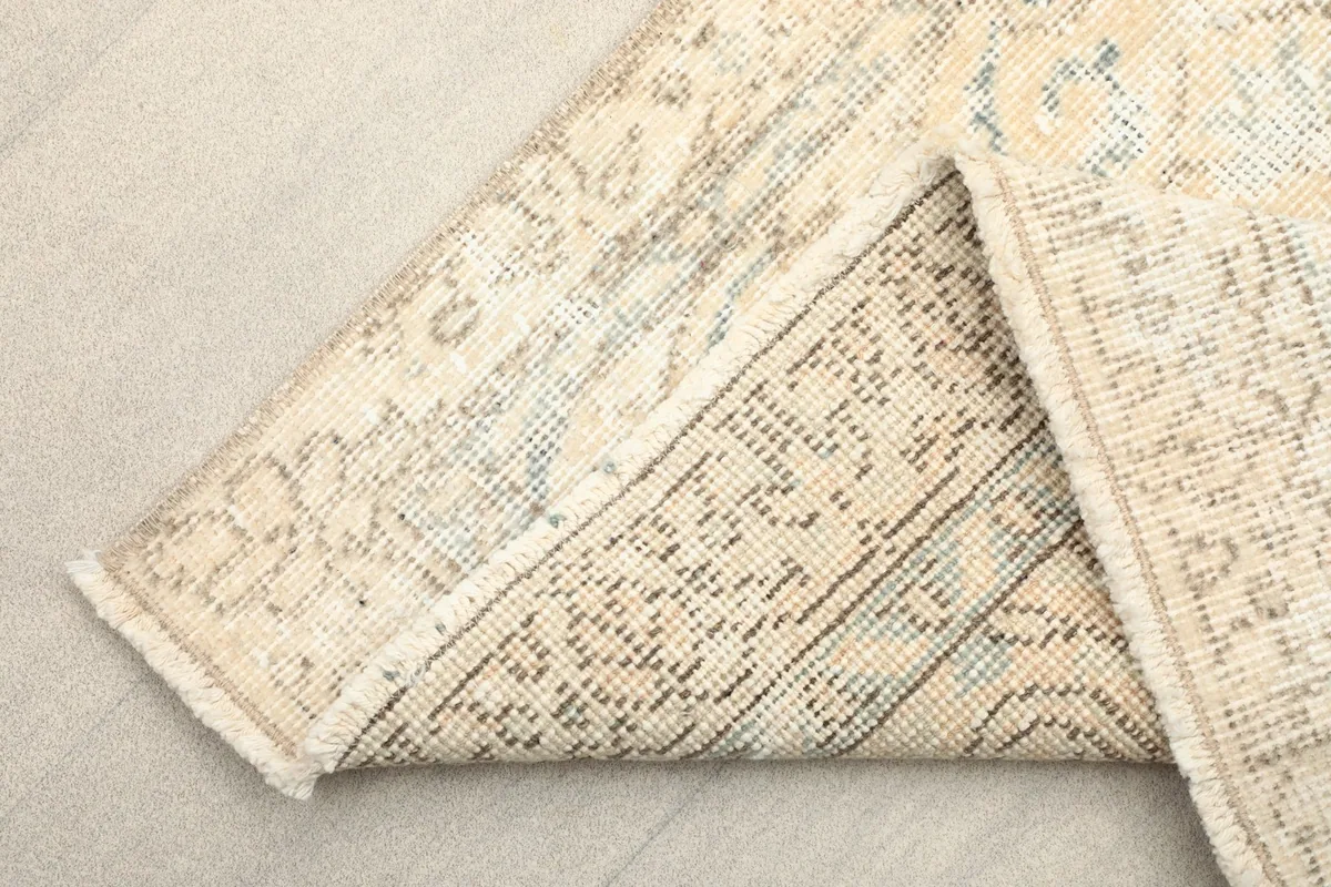 Corner of the rug folded to show the cotton foundation and reverse side of the hand-knotting.