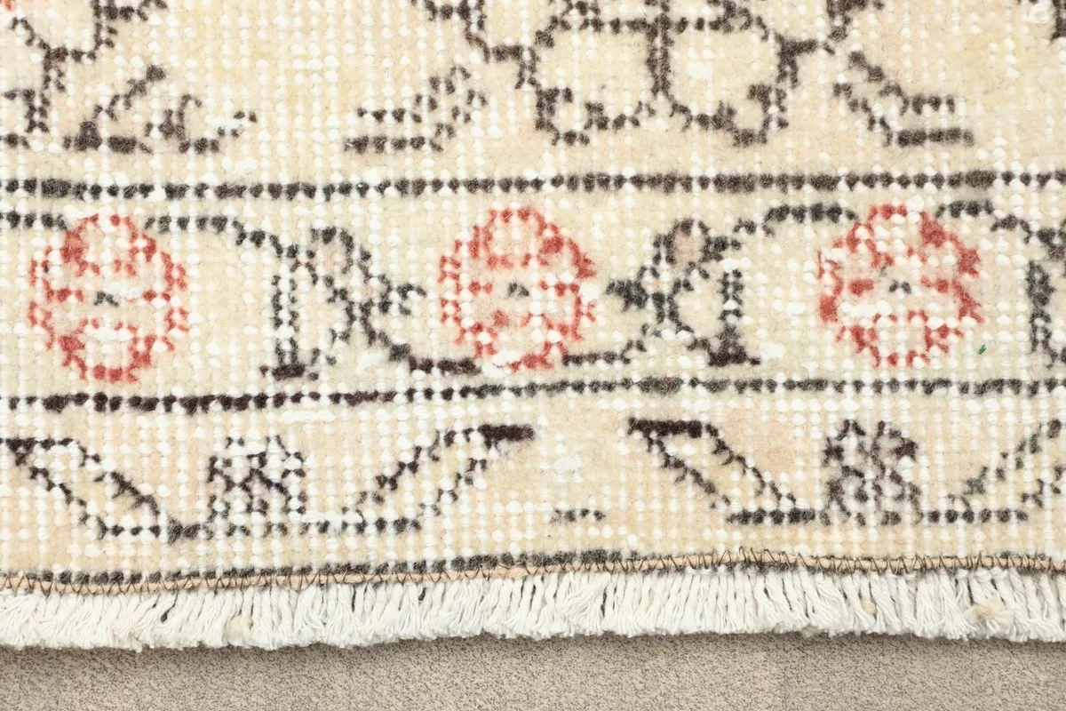 Close-up of the rug's border showing rose floral and gray geometric patterns with fringe