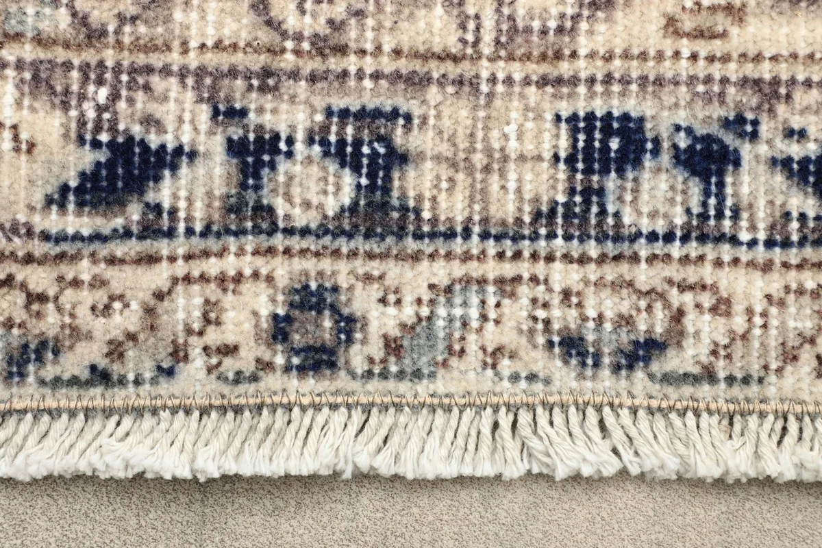 Close-up detail of the rug's border with navy blue accents and short fringe.