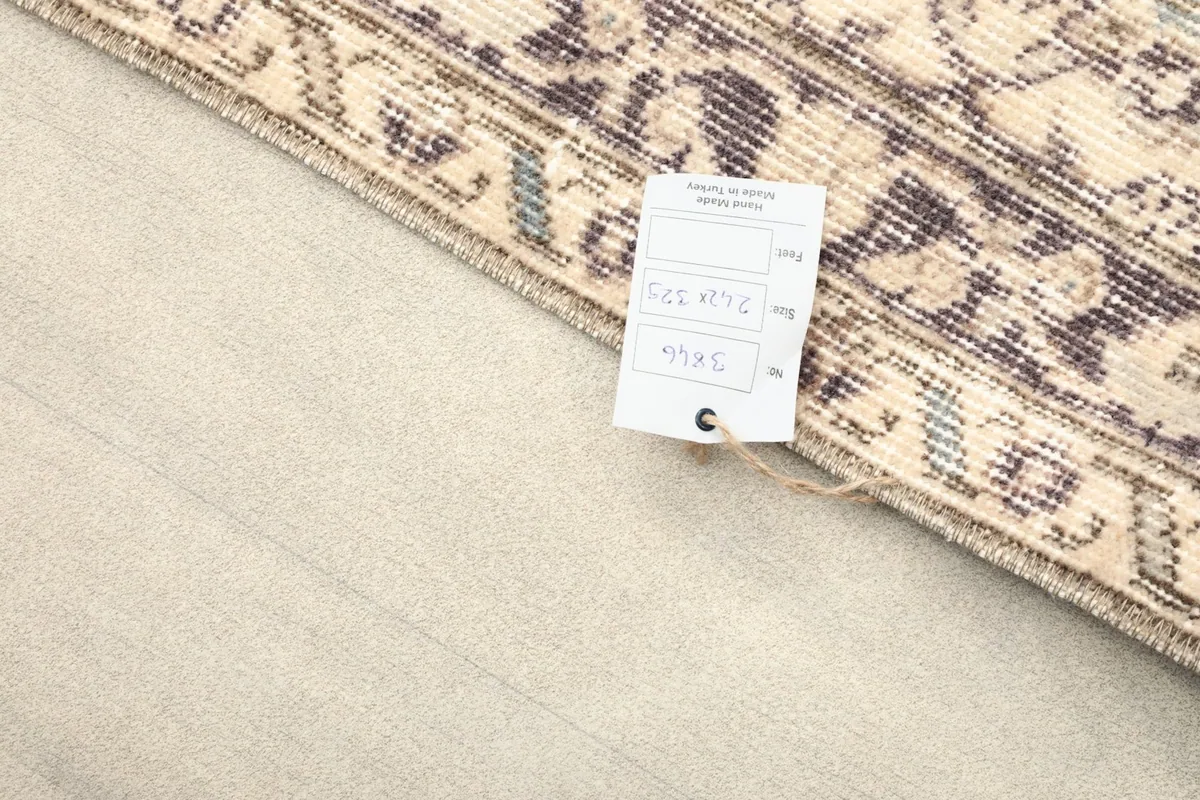 Rug corner with a product tag showing dimensions and item number, on a light wood floor.