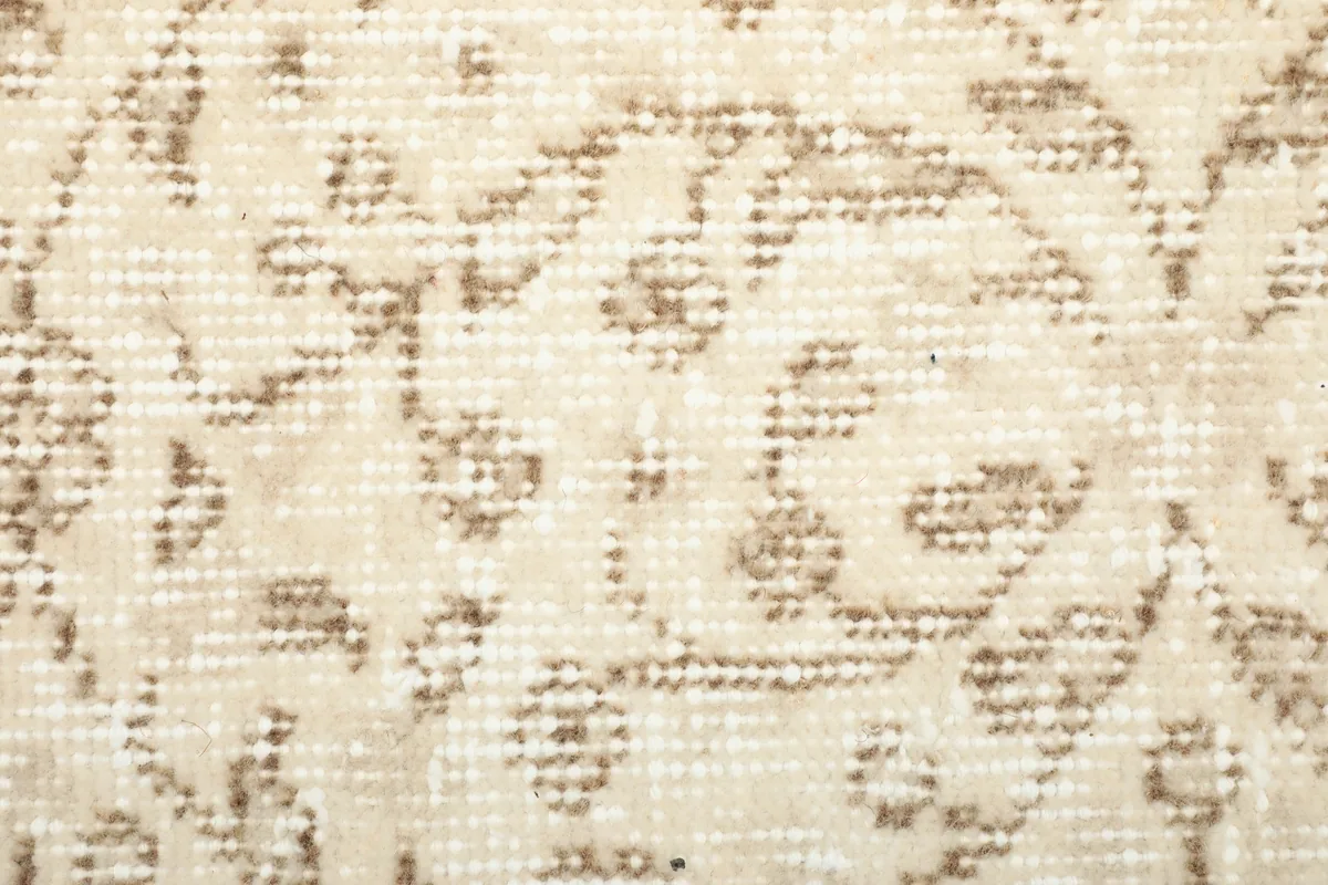 Close-up of the low wool pile and faded tan and brown motifs on the ivory and beige background of the rug.