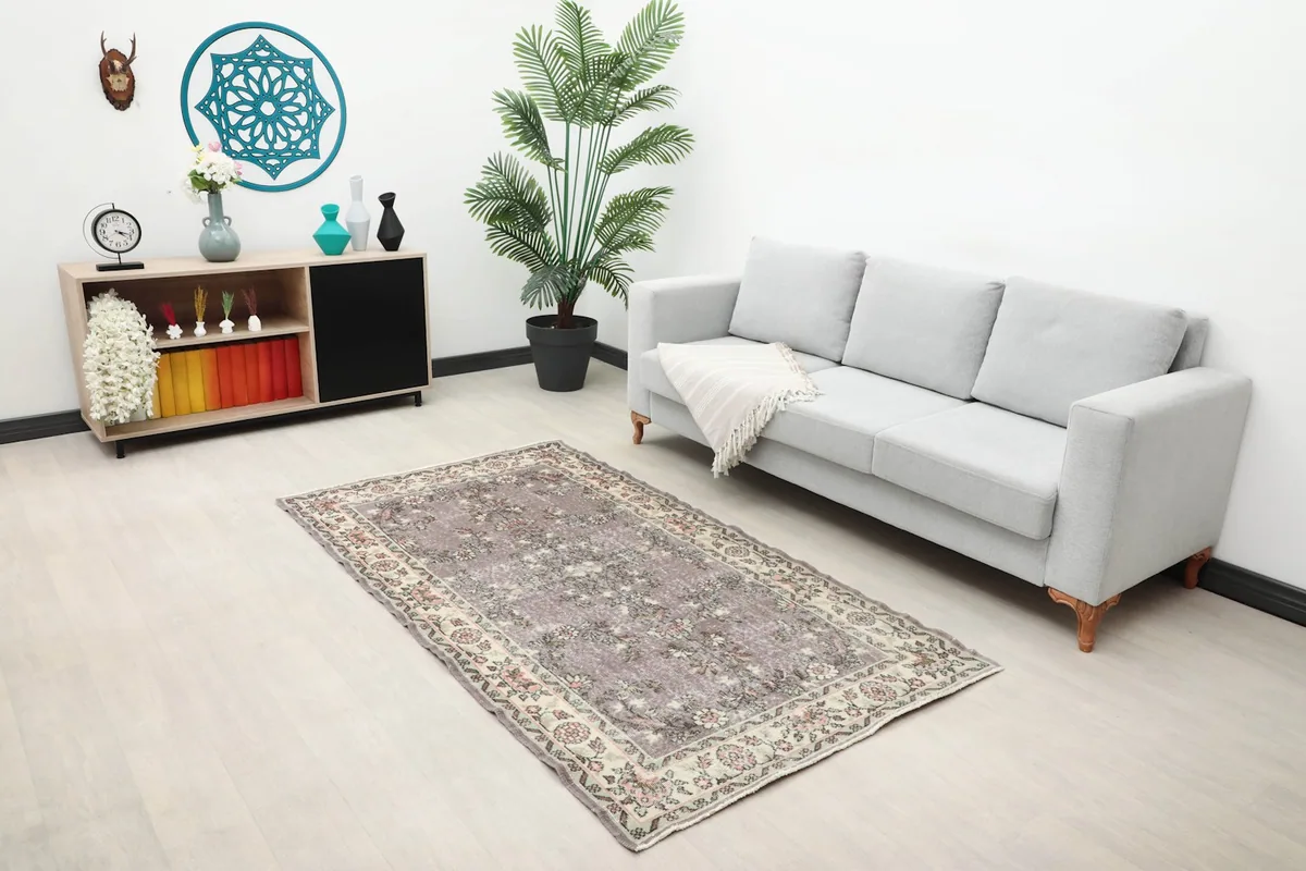 The purple floral rug placed in a living room setting under a gray sofa, showing scale.