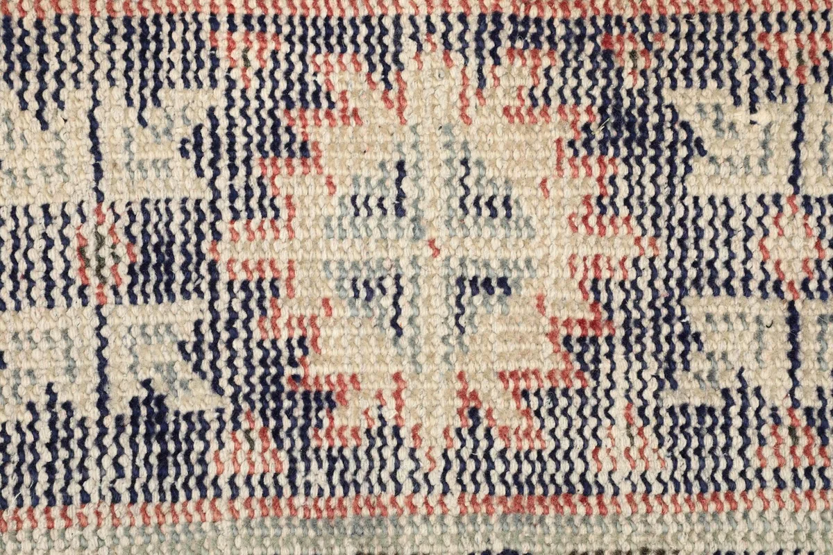 Close-up of the low wool pile, showing the texture and faded colors of the vintage rug
