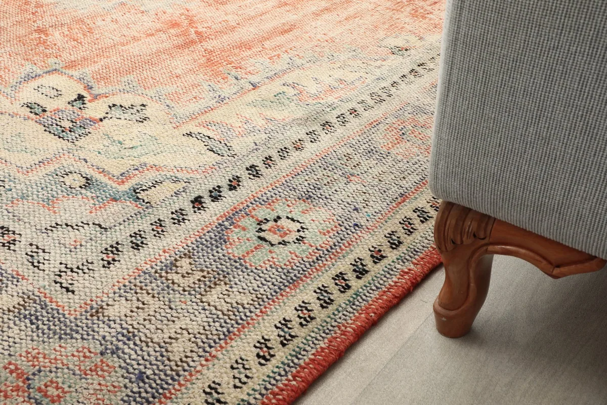 Detail of the rug's pattern and border next to a furniture leg in a room setting