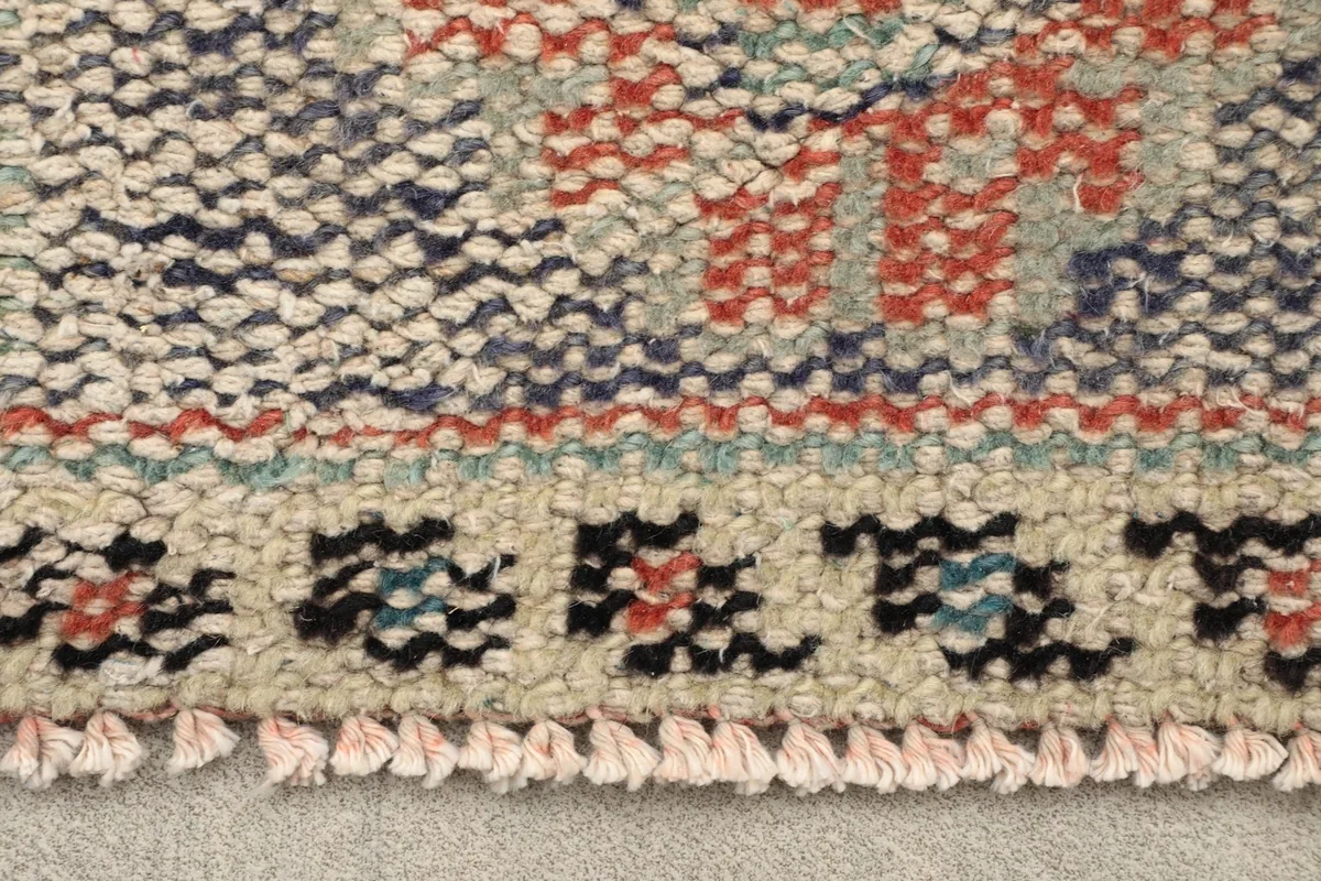 Close-up of the rug's edge showing fringe and intricate tribal patterns in rust, blue, and ivory
