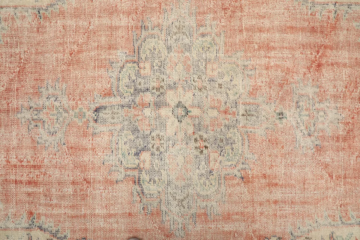 Close-up of the central medallion design on the rug, featuring faded rust and ivory colors