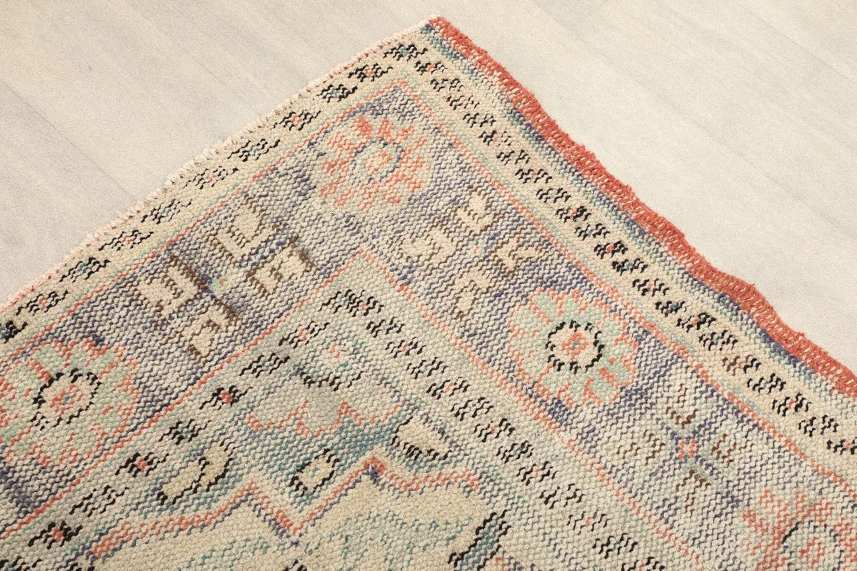Corner detail of the rug's border with geometric patterns in gray, blue, and rust tones