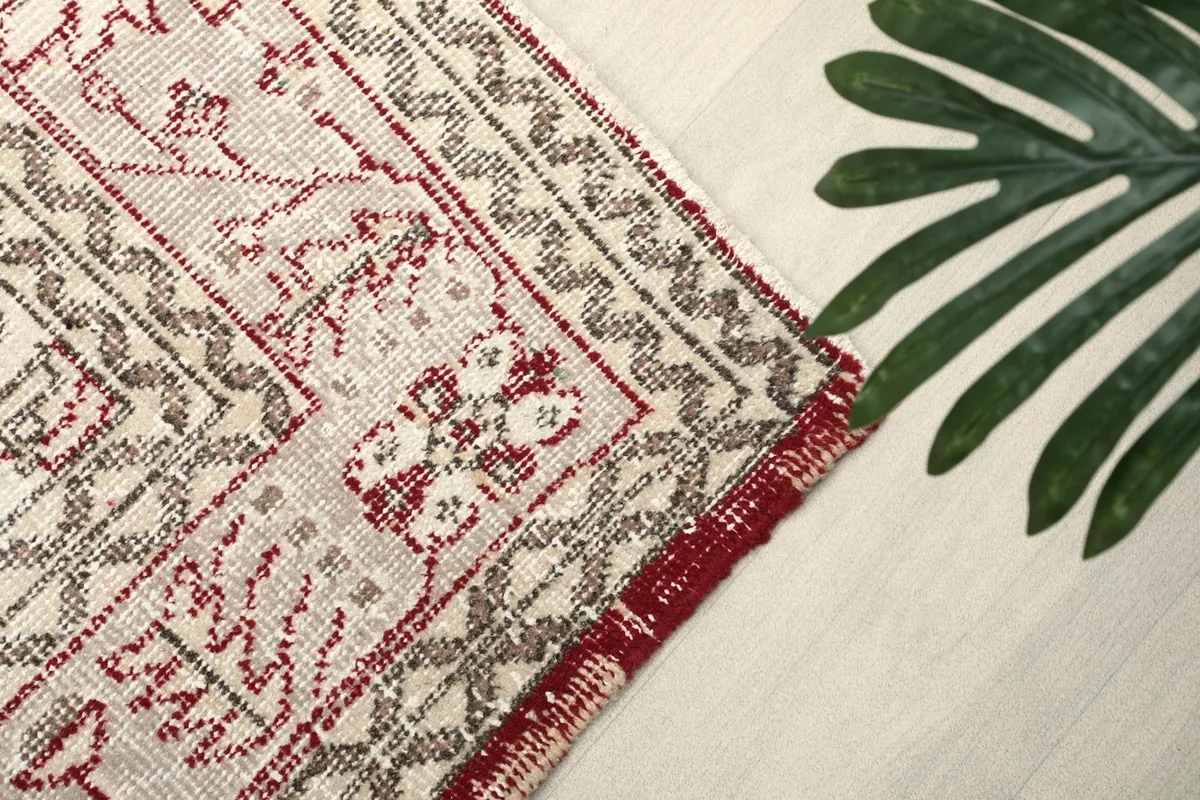 Close-up of the rug's border showing faded red, ivory, and gray tones with a green leaf accent