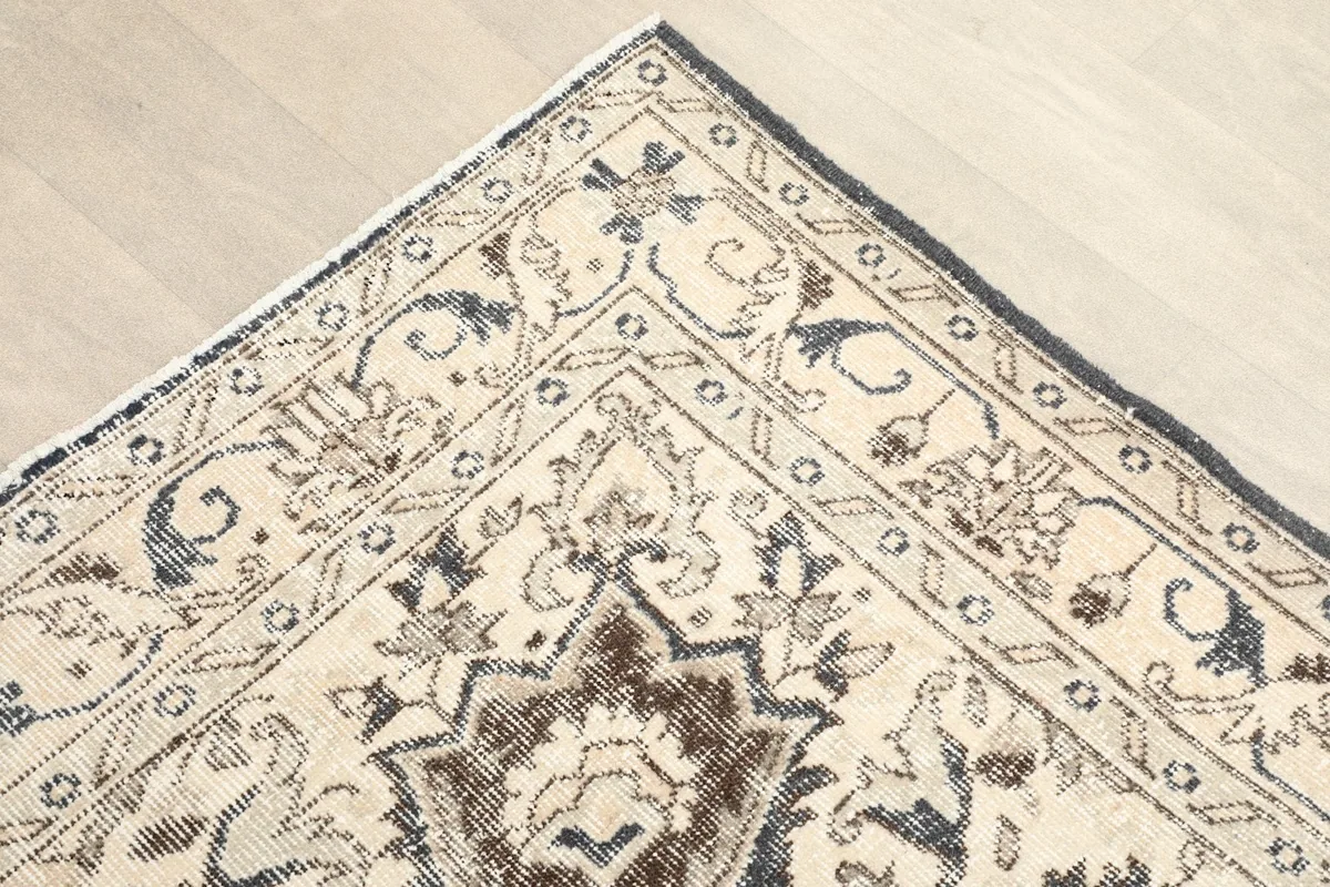 Corner view of the rug showing the ivory field, charcoal border, and subtle motifs