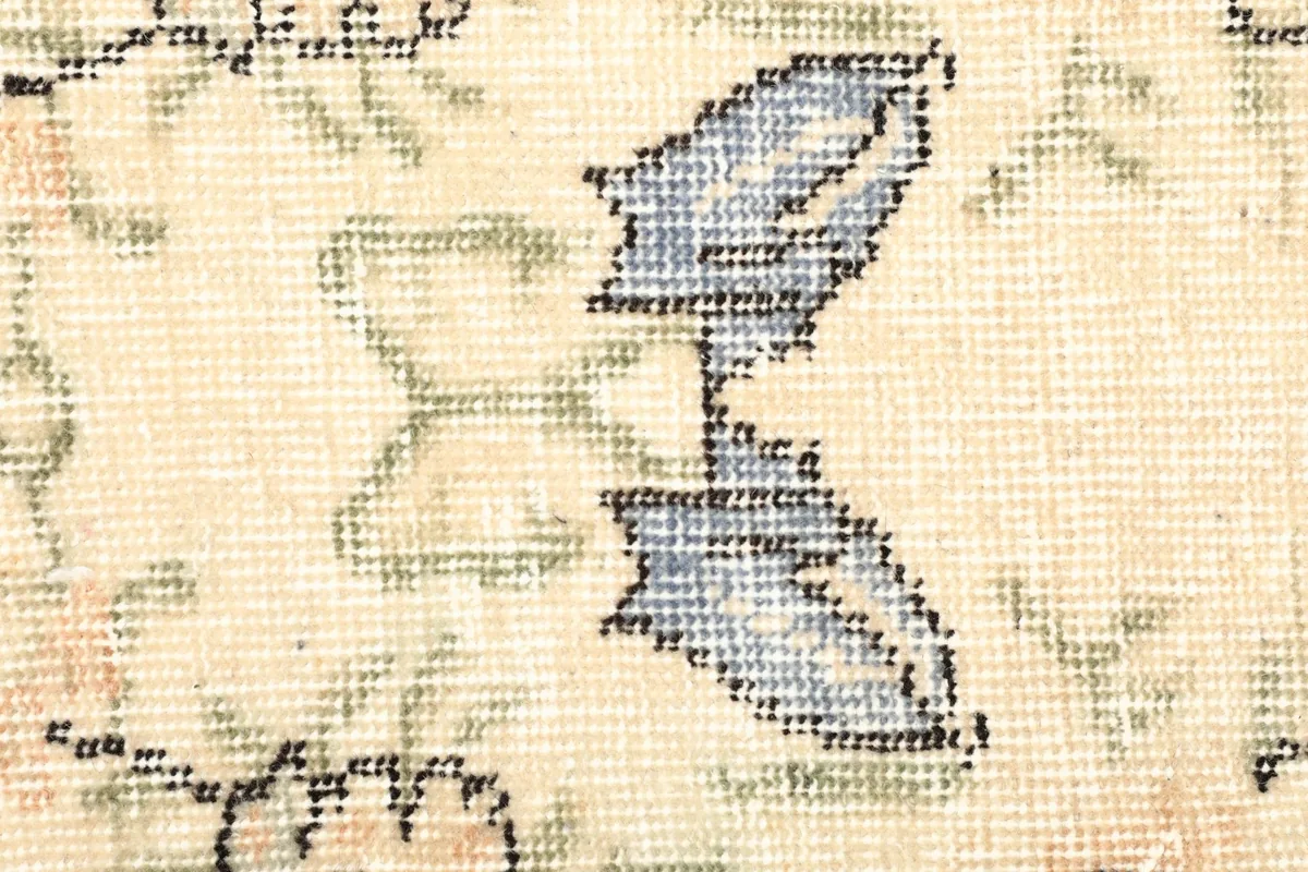 Close-up of a blue floral motif and green accents on the rug's cream field