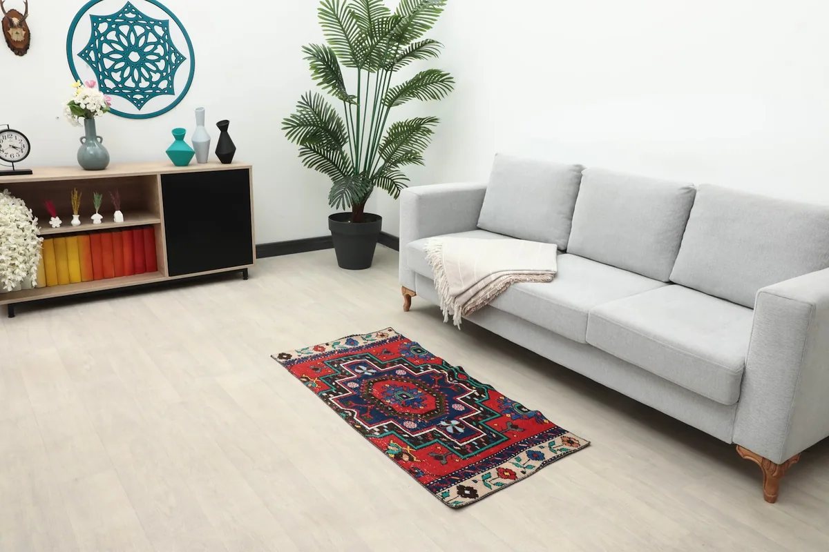 Vintage red and navy Anatolian rug placed in a modern living room setting next to a gray sofa.
