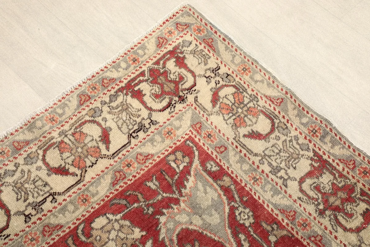 Corner view showing the intricate red and beige border design of the vintage rug