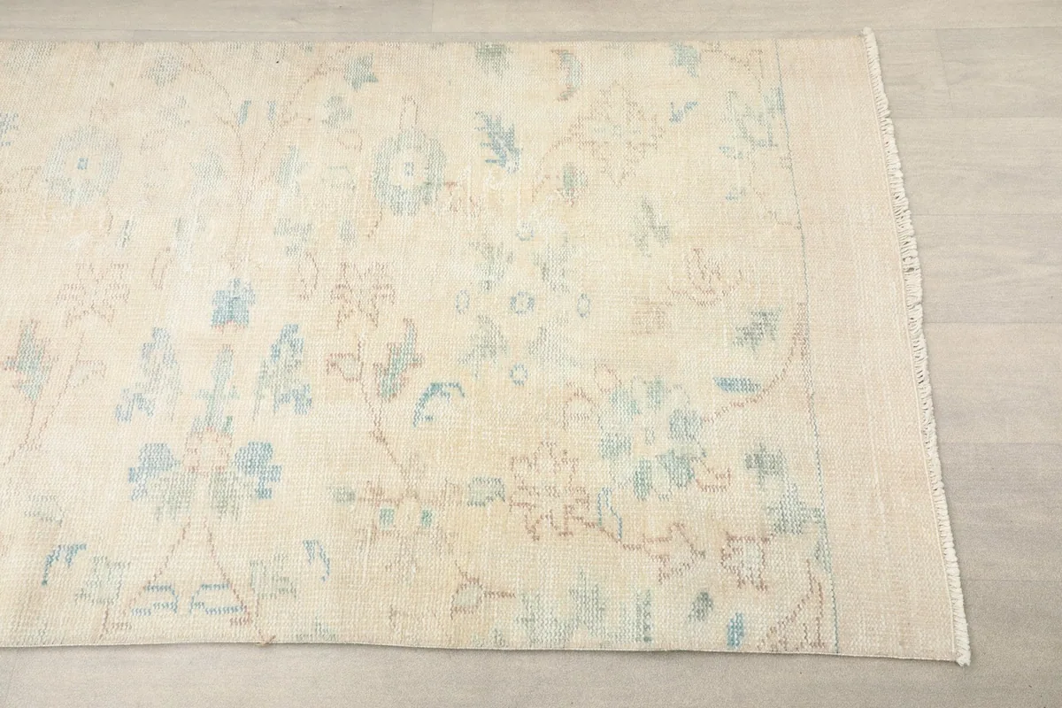 Close-up view of one end of the cream runner rug, highlighting the faded floral motifs and low pile.