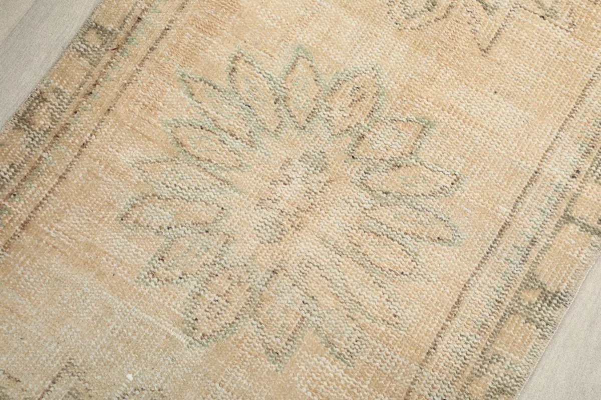 Close-up of a single gray medallion pattern against the beige background, showing worn pile