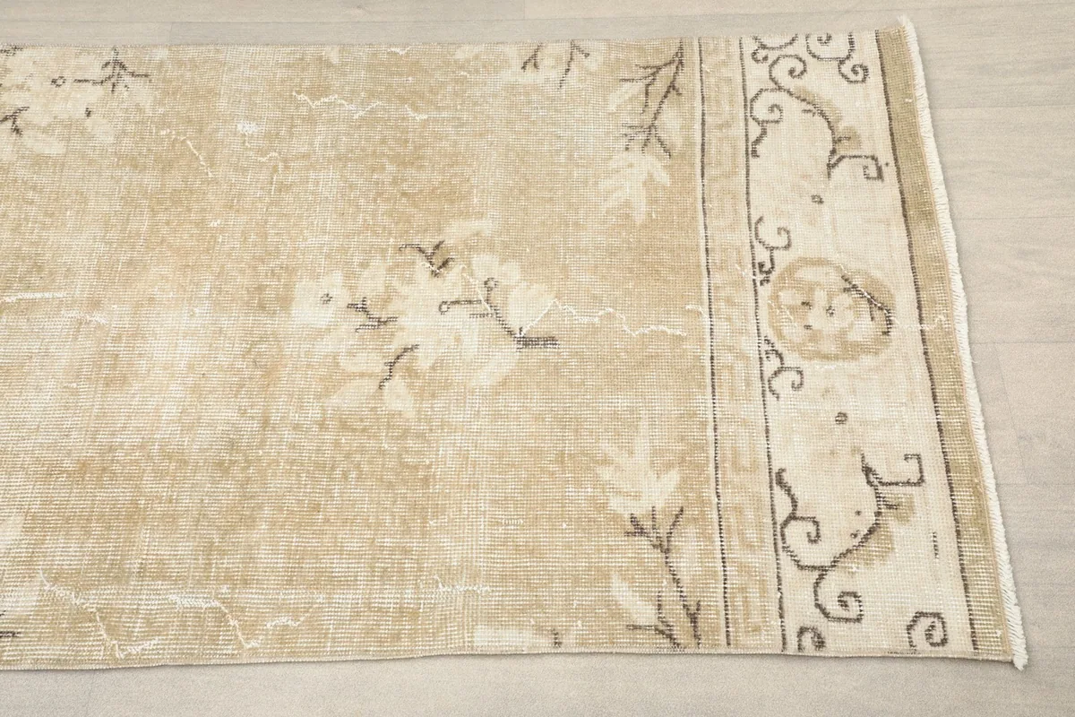 Close-up view of the rug's end, showing the beige field, floral motifs, and border design.