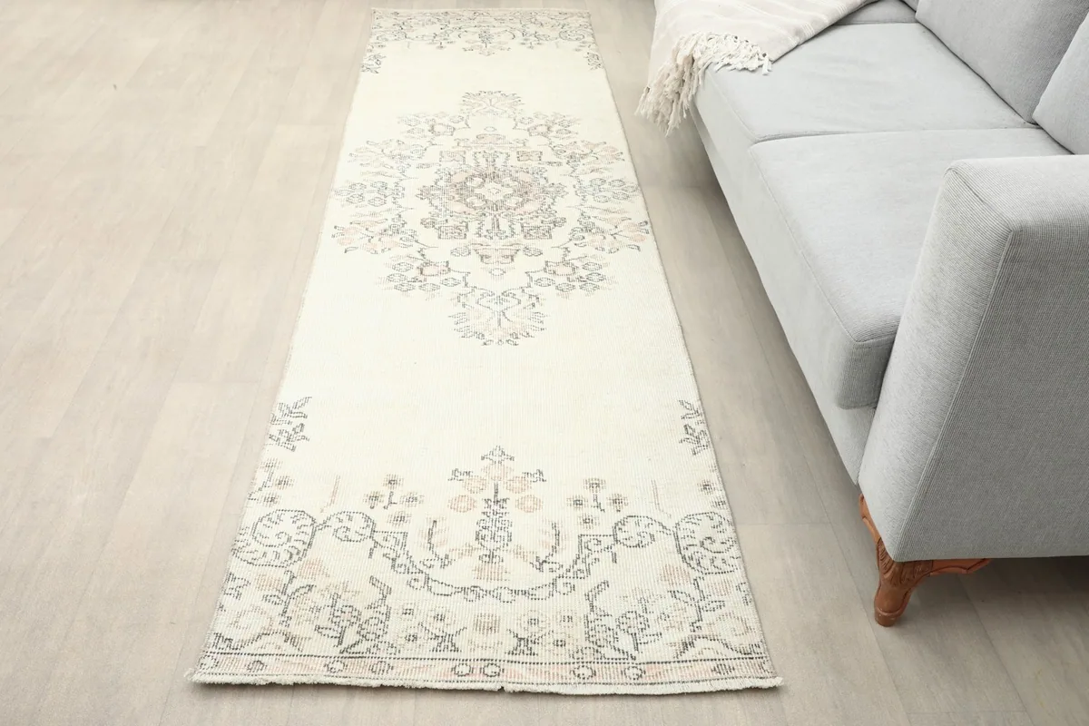 Vintage runner rug in an ivory and rose floral pattern placed alongside a gray sofa