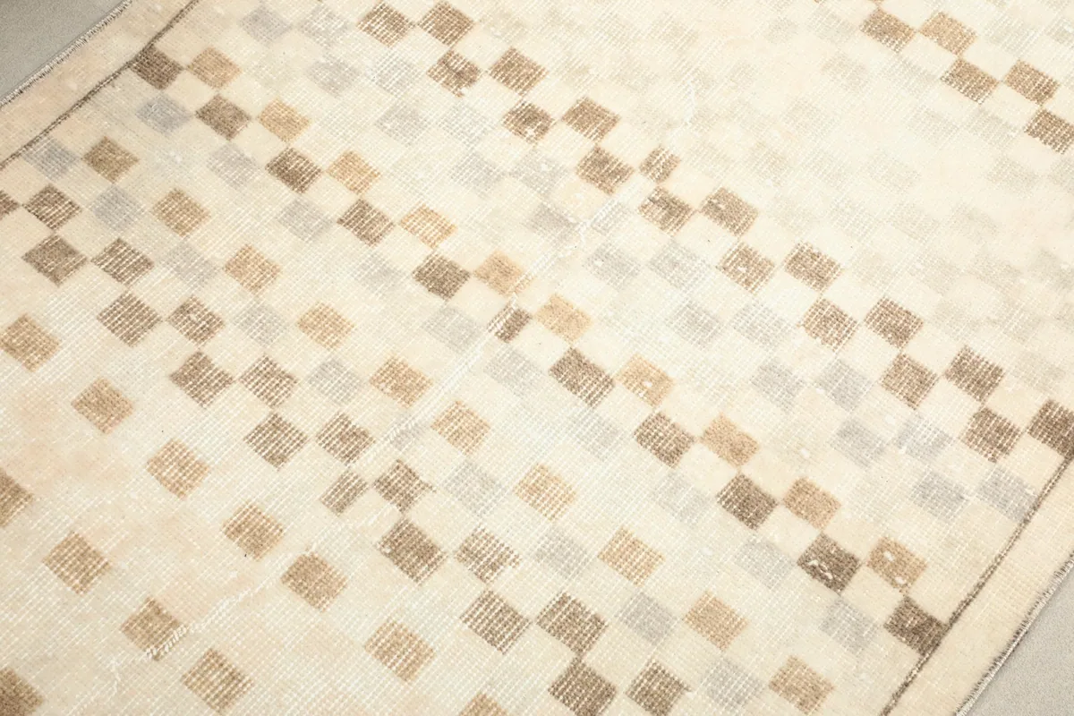 Detailed view of the hand-knotted geometric square pattern in beige, brown, and gray