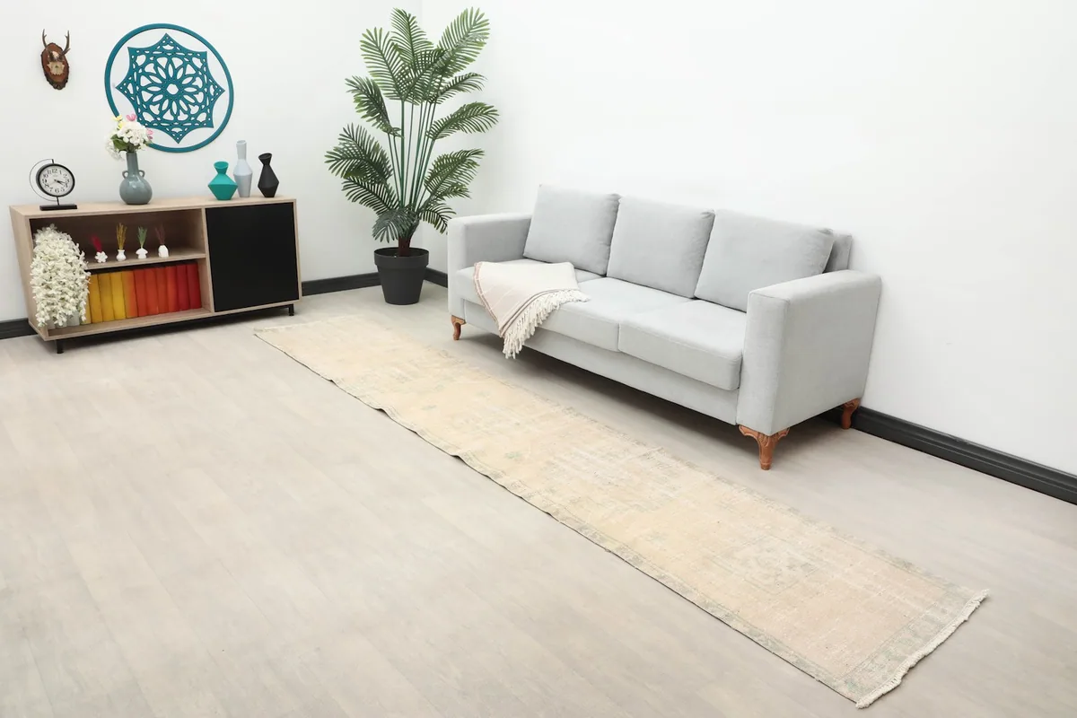 Long view of the ivory and green runner rug extending across a room with a sofa and side table.