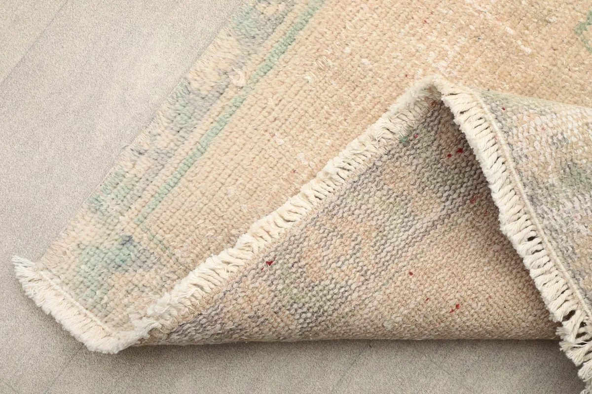 Corner of the rug folded to show the hand-knotted wool pile and the cotton foundation, with short fringes.