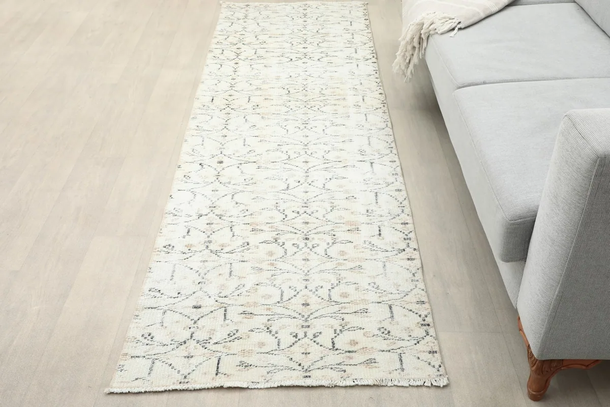 Ivory runner rug placed in a living room setting next to a gray sofa, showing its full length.