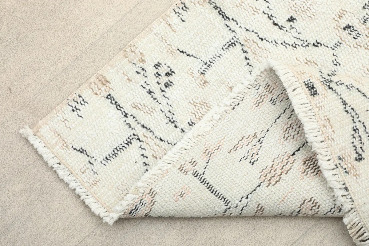 Corner of the rug folded back, revealing the fringe and the reverse side of the hand-knotted construction.