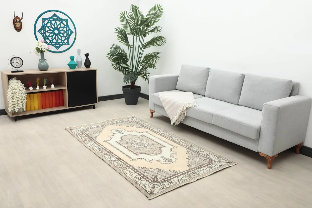 Beige and ivory vintage rug in a living room with a gray sofa and wooden cabinet
