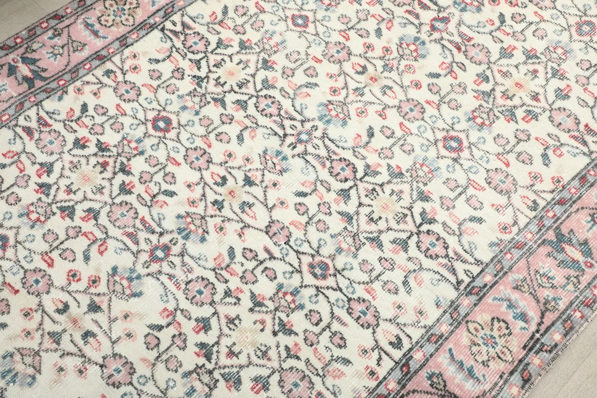Detailed view of the rug's hand-knotted floral motifs in rose, blue, and gray on an ivory background