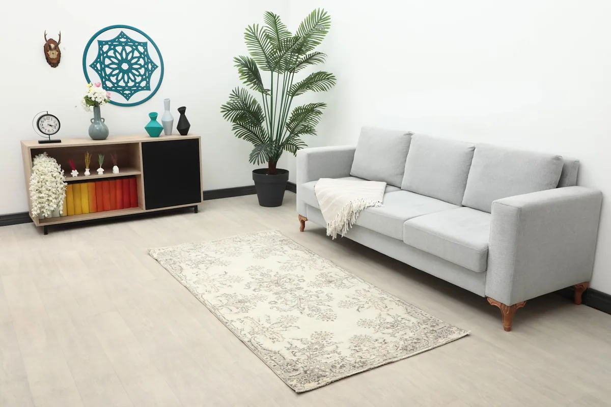 Ivory and gray floral rug placed in a modern living room with a gray sofa and wooden cabinet