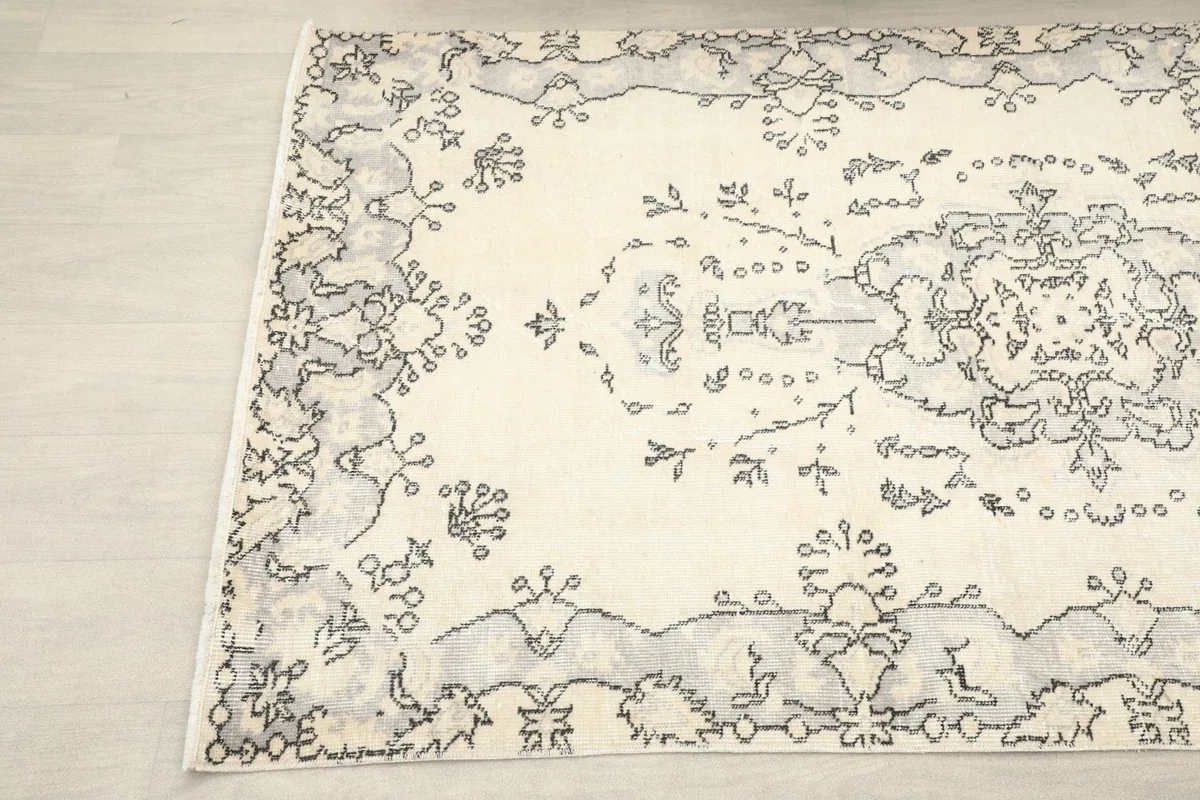 Angled view showcasing the intricate charcoal patterns against the ivory field of the rug.