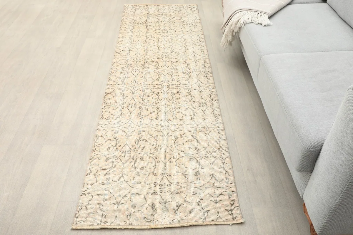 Beige runner rug laid out in a modern living space, viewed from an angle towards a gray sofa.