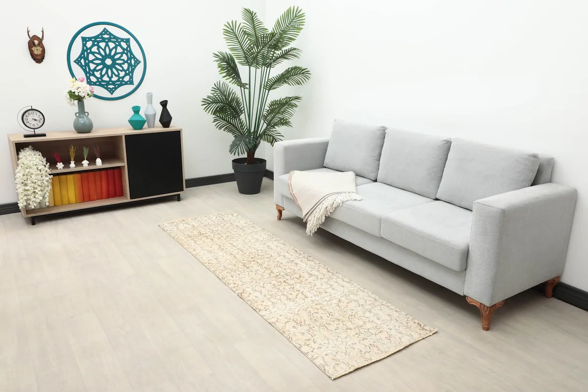 Wide shot of the beige runner rug in a room with a gray sofa, side table, and potted plant.