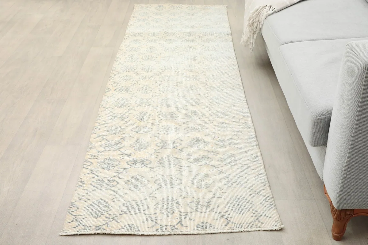 Vintage runner rug in an entryway next to a light gray sofa, showing its length and pattern.