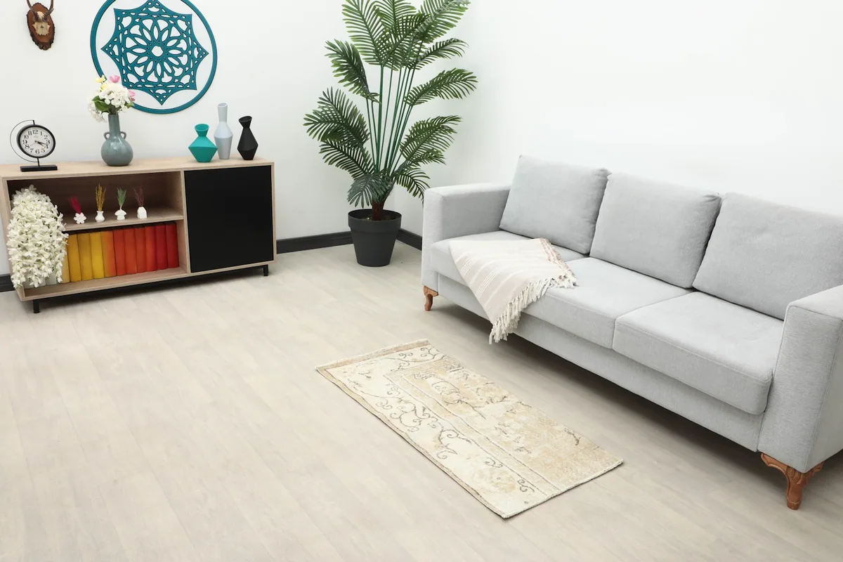 Vintage beige and brown rug placed in a living room setting next to a gray sofa and wooden cabinet.
